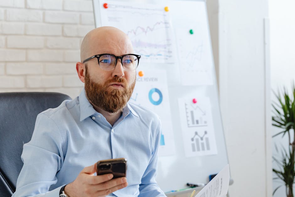 Bald man with beard holding smartphone in office setting, focused on business presentation.